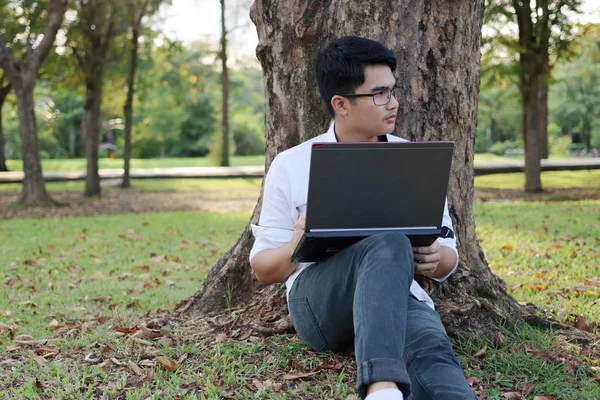 Potret pemuda tampan yang duduk di rumput hijau dengan laptop di taman . — Stok Foto