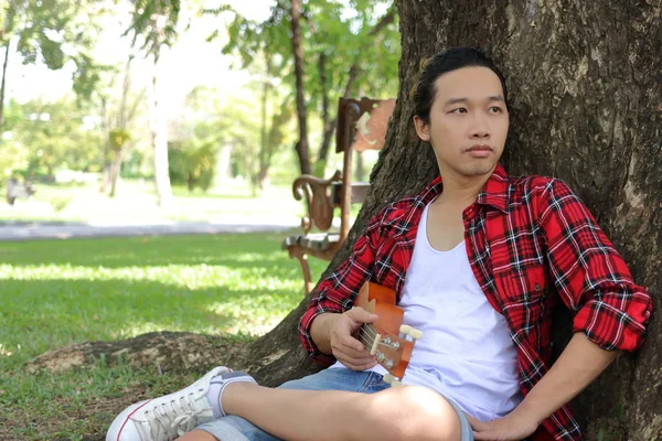 Portrét mladé bokovky člověka relaxační proti ukulele na pozadí přírody. — Stock fotografie