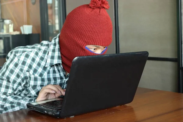 Masked hacker wearing a balaclava stealing important information data against laptop. Computer criminal concept. — Stock Photo, Image