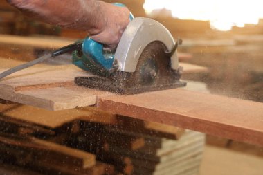 Seçici odak odun parçası üzerinde güneş etkisi arka plan ile doğrama atölyesinde çalışan eller karşı elektrik daire testere ile kesmek.