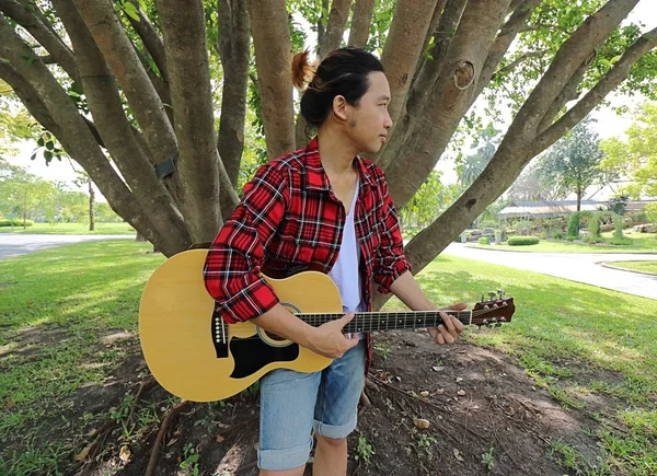 Amplo ângulo tiro de jovem homem relaxado tocando música na guitarra acústica em um belo fundo natureza . — Fotografia de Stock