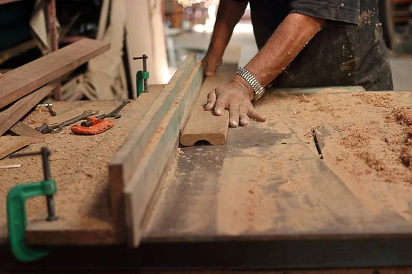 Stück Holzbrett wird auf einem Router-Tisch von den Händen eines leitenden Tischlers in der Tischlerei rasiert. Selektiver Fokus und geringe Schärfentiefe. — Stockfoto