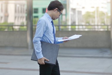 Yakışıklı genç Asya iş yan görünüm adam görünümlü evrak veya grafikler ofise yürüyüş arasında onun elinde