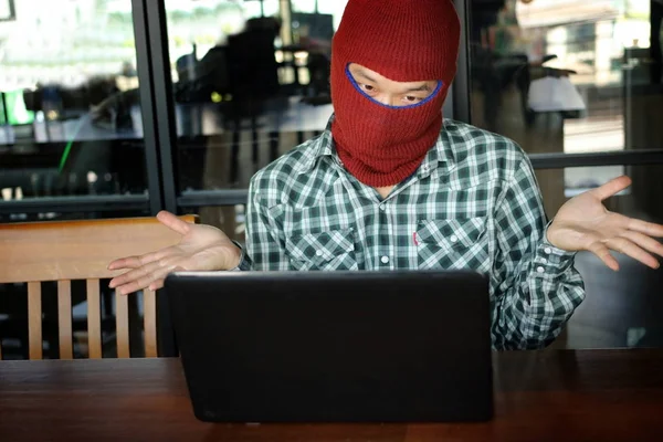 Maskerade hacker bär en balaclava som ser en laptop efter att stjäla viktig information data. Internet brottslighet koncept. — Stockfoto