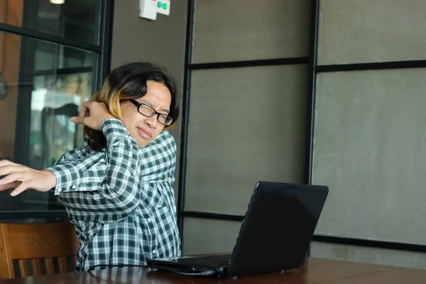 Lelah pemuda Asia hipster peregangan setelah bekerja keras dengan laptop di kantor . — Stok Foto