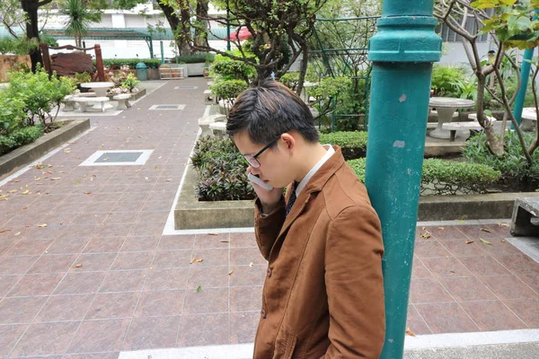屋外の公園で緑のポールをもたれながら携帯電話を使用してハンサムな若いビジネスマン. — ストック写真