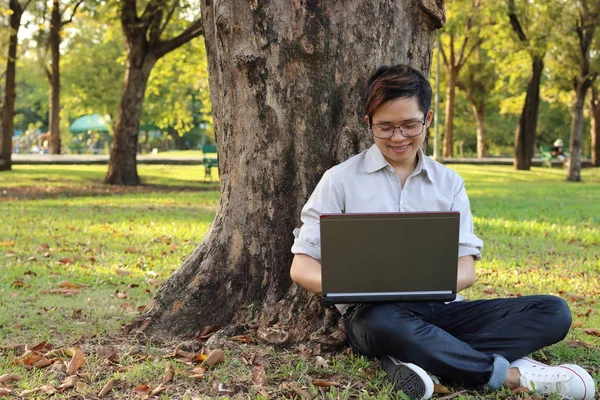 Young man sitting on green grass and enjoying with laptop in the park — Stock Photo, Image