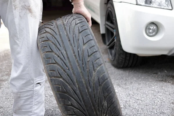 Foco seletivo nas mãos do mecânico automotivo em pneu uniforme para fixação de carro no fundo da garagem de reparação . — Fotografia de Stock