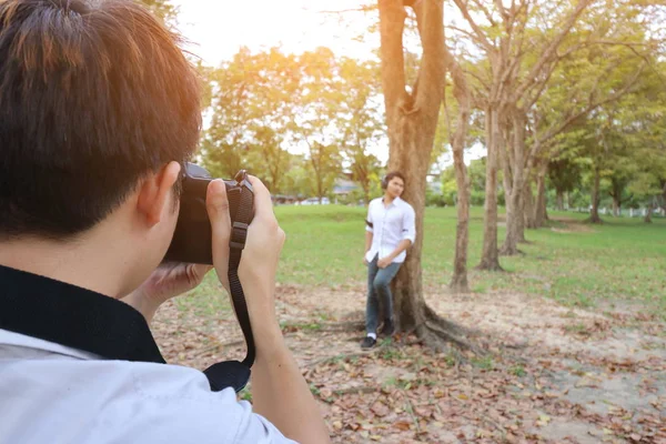 Back view of photographer taking a photo of young man in summer park. Sunshine effect. Vintage tone/ — Stockfoto