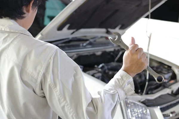 Vista posteriore di professionale giovane meccanico in uniforme tenuta chiave contro auto in cappa aperta presso il garage di riparazione . — Foto Stock