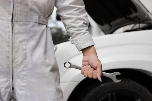Manos del hombre mecánico profesional en uniforme blanco que sostiene la llave con el coche en la capucha abierta en el fondo del garaje de reparación . —  Fotos de Stock