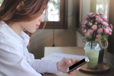 Çekici genç Asya iş kadın görünümlü mobil akıllı telefon onu yan görünümü kahve kafede eller.