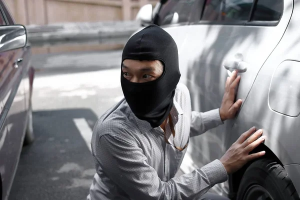 Masked burglar wearing a balaclava ready to burglary against car background. Insurance crime concept. — Stock Photo, Image