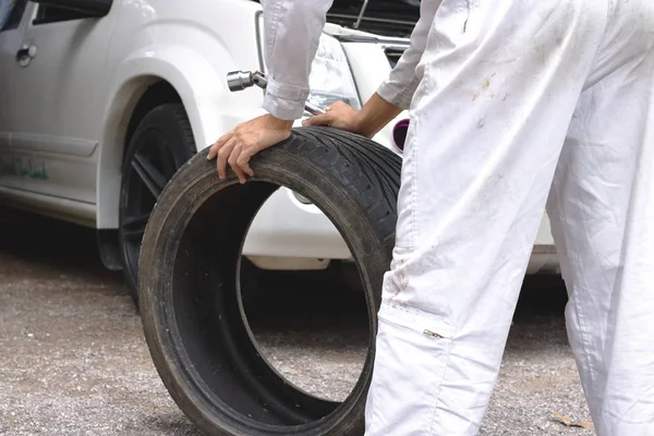 Mãos de mecânico em uniforme branco segurando pneu no fundo da garagem de reparação. Conceito de serviço de carro . — Fotografia de Stock