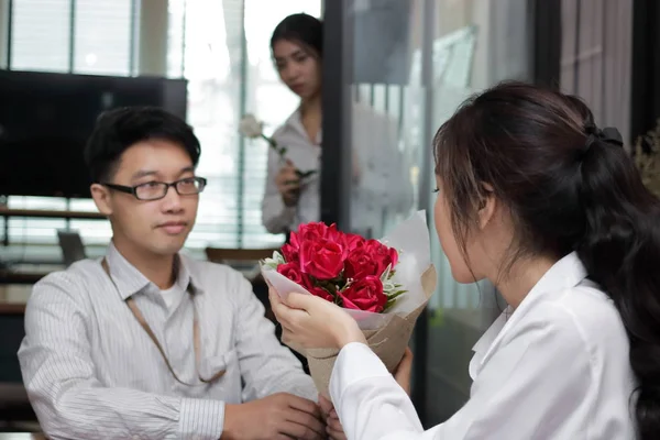 Joyeux jeune femme asiatique acceptant un bouquet de roses rouges de petit ami avec fond envieux femme en colère le jour de la Saint-Valentin. Amour et romance en milieu de travail concept . — Photo