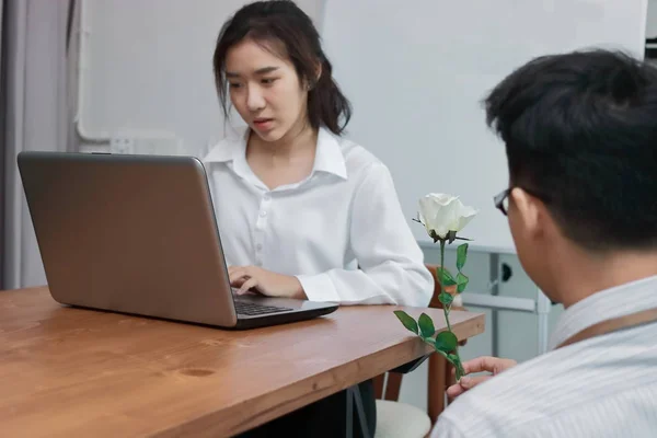 Привлекательная молодая азиатка, работающая с ноутбуком, с бизнесменом, дарящим белую розу в офисе на день Святого Валентина. Любовь и романтика в концепции рабочего места . — стоковое фото