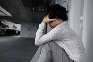 Hayal kırıklığına uğramış yorgun genç Asya iş adamı arka görünümü oturur ve dizlerinin kadar göğüs sarılarak