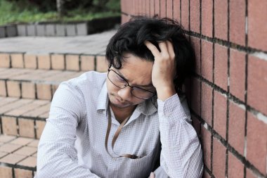 Hayal kırıklığına uğramış genç Asyalı adam kafa dokunmaktan ve hayal kırıklığına veya yorgun hissediyorum vurguladı. İşsiz işadamı kavramı.