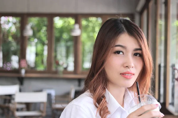 Close up attractive young Asian woman holding coffee cup and looking to camera at cafe with copy space background. — Stock Photo, Image