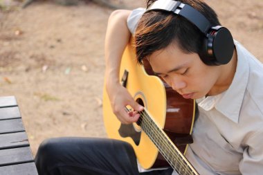 Seçici odak rahat gencin içinde açık akustik gitar çalıyor.