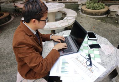 Genç bir işçi dizüstü bilgisayar boş ekran, evrak ve cep telefonu ile çalışmaları için kullanıyor.