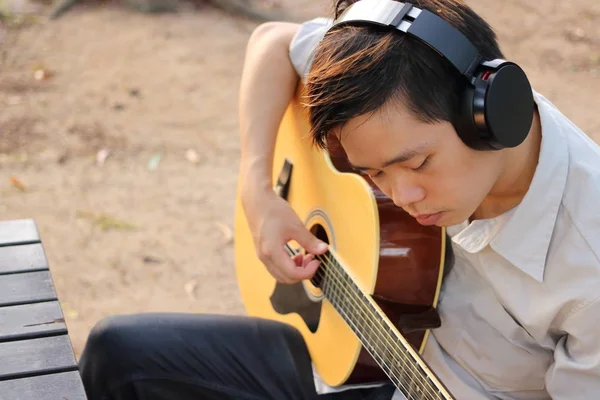 Foco seletivo do jovem homem relaxado está tocando guitarra acústica ao ar livre . — Fotografia de Stock