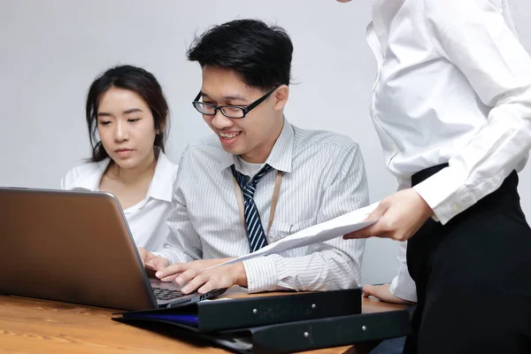 Young Asian business people working together on a laptop computer at office. Teamwork brainstroming concept. Selective focus and shallow depth of field.