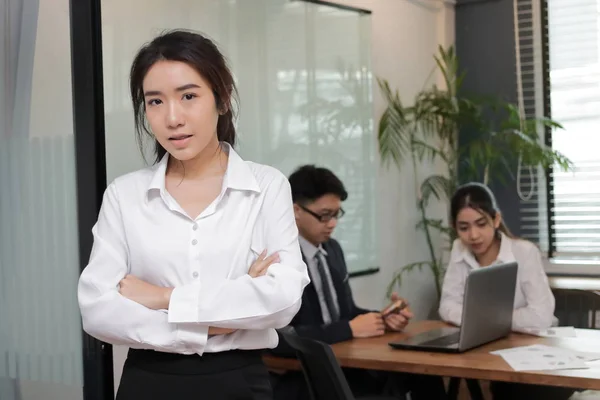 Портрет уверенной молодой азиатской бизнес-женщины, стоящей в офисе с коллегами в фоновом режиме конференц-зала . — стоковое фото