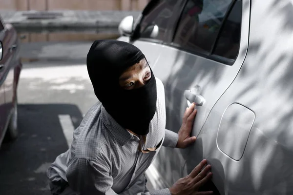 Ladrão mascarado usando uma balaclava pronto para assaltar contra o fundo do carro. Conceito de crime de seguro . — Fotografia de Stock