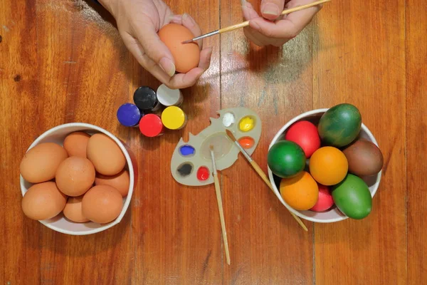 Vista superior de las manos de los jóvenes para colorear huevos de Pascua con un pincel en la parte superior de madera . — Foto de Stock