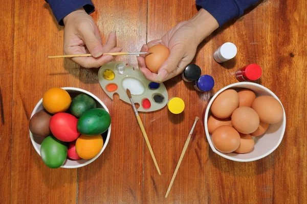 Верхний вид красочных пасхальных яиц раскрашивают кистью и палитрой молодого человека на деревянном столе . — стоковое фото
