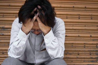 Sinirli stresli genç Asya iş adamı kafa dokunmaktan ve hayal kırıklığına veya iş ile yorgun hissediyorum elle önden görünümü.