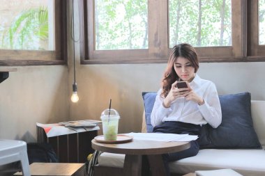 Çekici genç Asyalı kadın kahve dükkanında seyir mobil akıllı telefon önden görünümü.