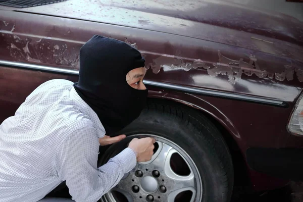 Masked burglar wearing a balaclava ready to burglary against car background. Insurance crime concept. — Stock Photo, Image