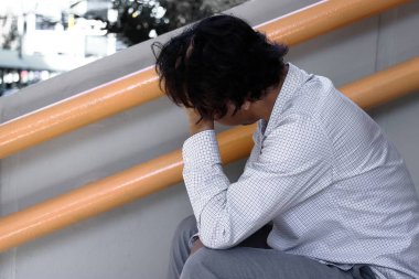 Asya iş adamı depresyon merdiven üzerinde oturan alnına elleriyle vurguladı