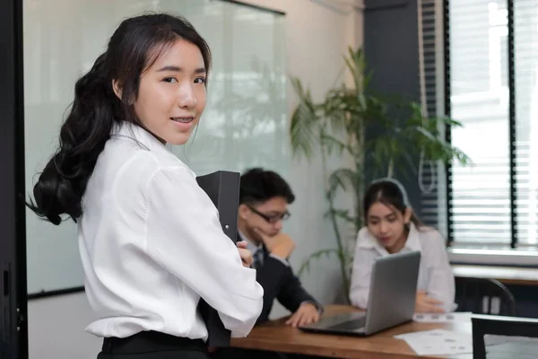 Лидерство молодая азиатская деловая женщина с кольцом папки стоя против своего коллеги в офисе фоне . — стоковое фото