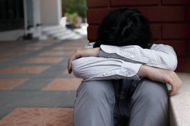 Asya iş adamı oturur ve dizleri göğsüne kadar sarılarak overworked genç yorgun