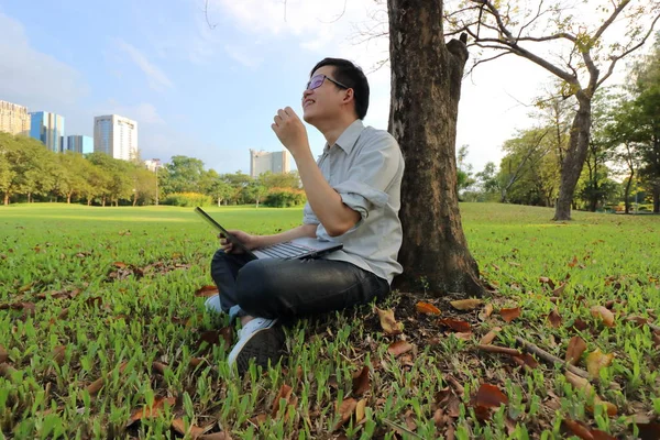 Vidvinkel skott av glad ung man skrattar med en bärbar dator i stadsparken. — Stockfoto