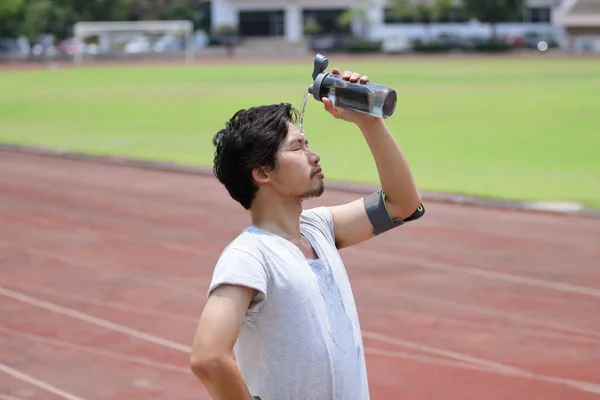 Guapo joven asiático fitness hombre salpicando agua en su cara después de ejecutar en pista de estadio . — Foto de Stock