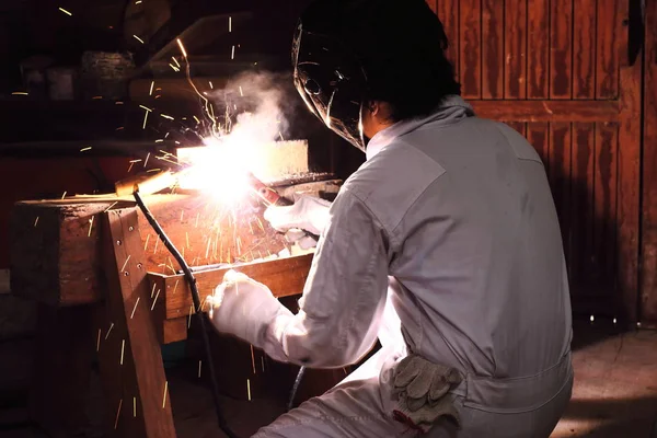 Seitenansicht eines professionellen Schweißers in Arbeitskleidung, der Stahl mit Funken in der Werkstatt schweißt. Industriekonzept. — Stockfoto