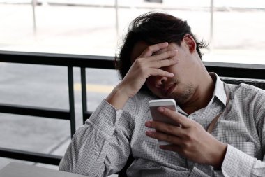 Depresif Asya iş adamı elle seyir mobil akıllı telefon ofis onun elinde alnına.