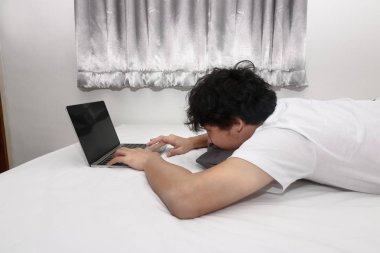 Yorgun genç Asyalı adam yatağa laptop ile çalışma