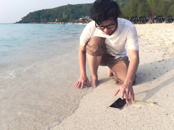 Joven hombre asiático dejando caer el teléfono inteligente móvil en la playa de arena tropical. Concepto de equipo electrónico de accidentes y seguros — Foto de Stock