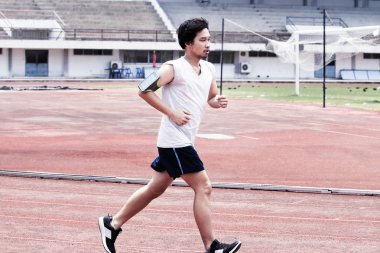 Yakışıklı sporcu Asya adam stadyumda yarış pisti üzerinde çalışan dramatik tonda görüntüsü. Sağlıklı aktif yaşam tarzı kavramı.