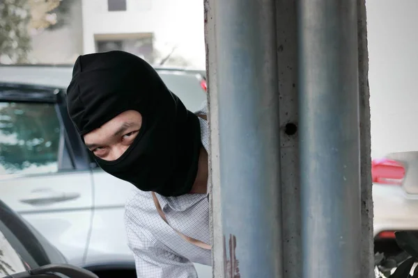 Ladrão mascarado escondido atrás de um poste antes do assalto. Conceito criminoso de ladrão de carros . — Fotografia de Stock