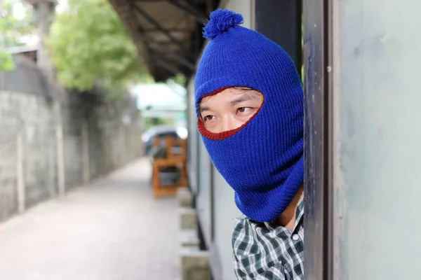 Un ladrón enmascarado que llevaba un pasamontañas escondido detrás de un poste antes del robo. Concepto de crimen — Foto de Stock