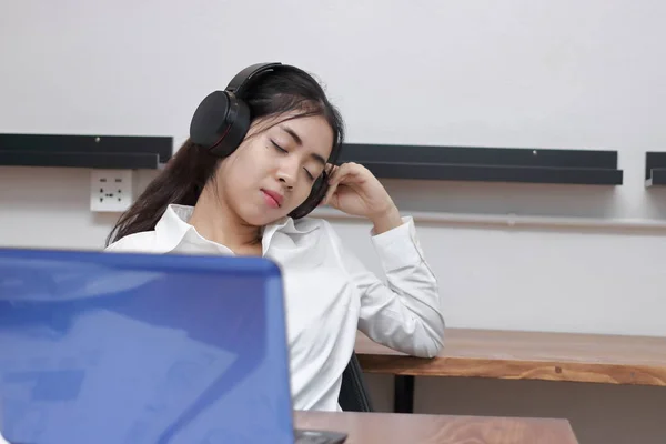 Bijgesneden afbeelding van ontspannen jonge Aziatische zakenvrouw iemands ogen dicht en luisteren muziek met koptelefoon op werkplek. — Stockfoto