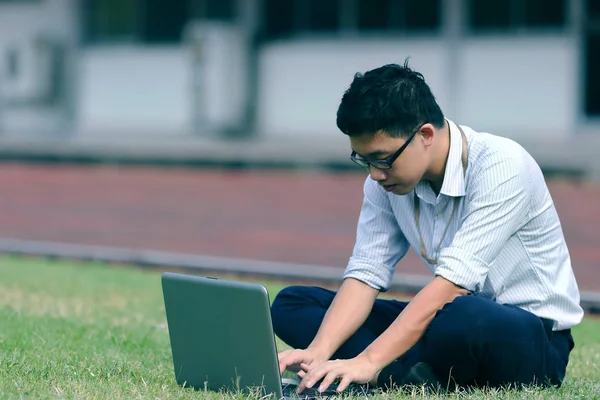 Vintage tonas bild av avslappnad unga asiatiska företag man arbetar med laptop på grönt gräs. — Stockfoto