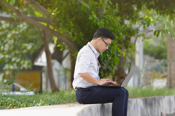 Portrait of confident young Asian business man working with laptop at public park. — Stock Photo, Image