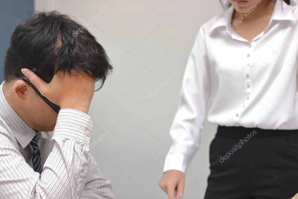 Angry woman boss blaming young Asian man with hands on face in office.